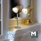 1:12 scale miniature standing crucifix in silver on a stepped base, shown on a white fireplace mantel beside a lamp