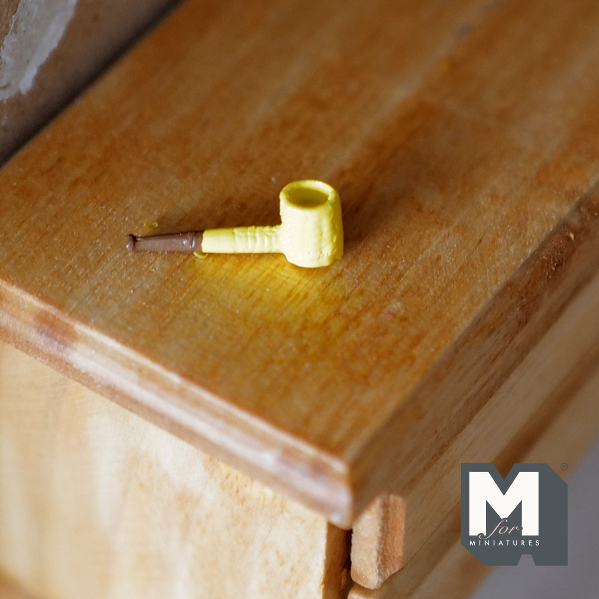 1:12 scale miniature metal corn cob pipe with yellow bowl and brown stem, shown on a wood dresser