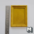 1:12 scale miniature gold rectangular picture frame with molded border, shown beside a ruler on a gray surface