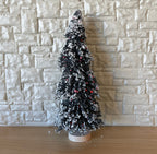 1:12 scale miniature snowy pine tree with base, medium, green and white with red berries, shown against a stone wall