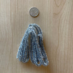 1:12 scale miniature silver tinsel garland, cut to length, shown looped in a bundle on wood beside a coin for scale