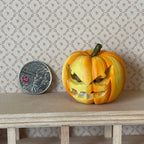 1:12 scale miniature carved pumpkin in orange with an angry face, shown beside a coin on a wood shelf