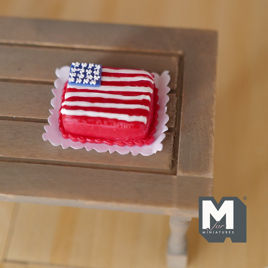 1:12 scale miniature clay American flag cake with red and white stripes on a white doily, shown on a wood table
