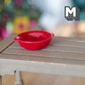 1:12 scale miniature salad bowl in red with two side handles, round and shallow, shown on a gray wood garden table