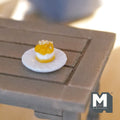 1:12 scale miniature cream puff with white plate, yellow topping and cream filling, shown on a gray wood table