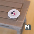 1:12 scale miniature blueberry pie on white scalloped plate, topped with berries and cream, on a gray wood table