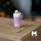1:12 scale miniature lavender milkshake in a glass with whipped cream and chocolate sauce, on a wood table