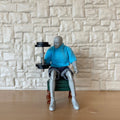 1:12 scale miniature black dumbbell with 4 removable plates, lifted by a seated artist figure by a stone wall