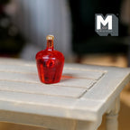 1:12 scale miniature red Bocksbeutel wine bottle with flat round shape, translucent, shown on a whitewashed table