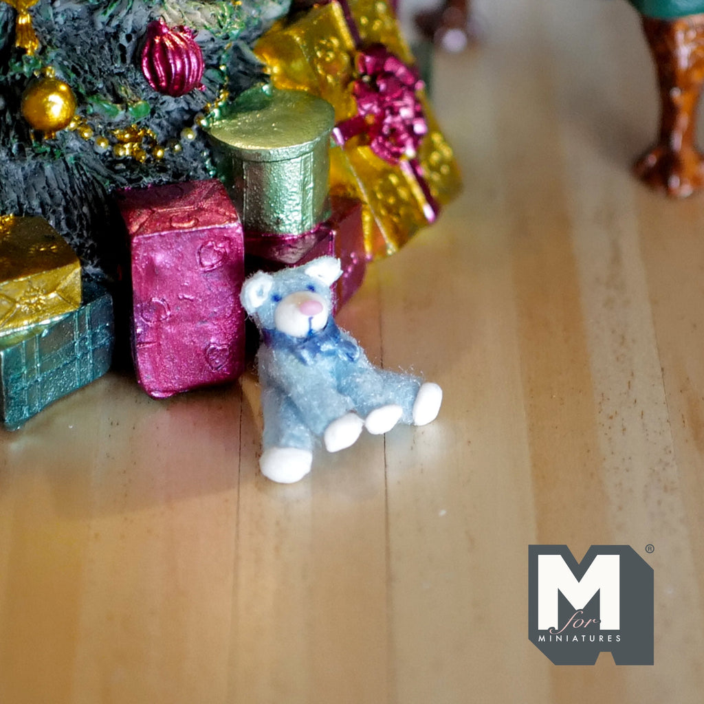 1:12 scale miniature blue plush sitting bear with ribbon, shown on a wood floor beside wrapped gifts under a tree