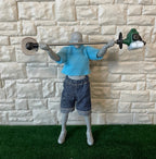 1:12 scale miniature straight shaft grass trimmer in green, non working, shown held overhead by an artist figure