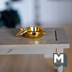 1:12 scale miniature metal shallow cooking pot in gold with lid and 2 side handles, shown on a gray wood table