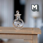 1:12 scale miniature clear glass wine decanter with ball stopper, flat round body, shown on a wood table