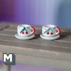 1:12 scale miniature ceramic cups and saucers with cherries and red handles, set of 4, shown on a wood plank table