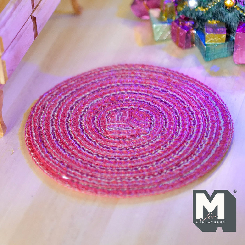 1:12 scale miniature round braided area rug in red and pink with white stitching, shown on a light wood floor