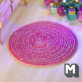 1:12 scale miniature round braided area rug in red and pink with white stitching, shown on a light wood floor