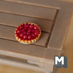 1:12 scale miniature cherry pie on a metal plate with glossy red cherries and a crimped crust, shown on a wood table