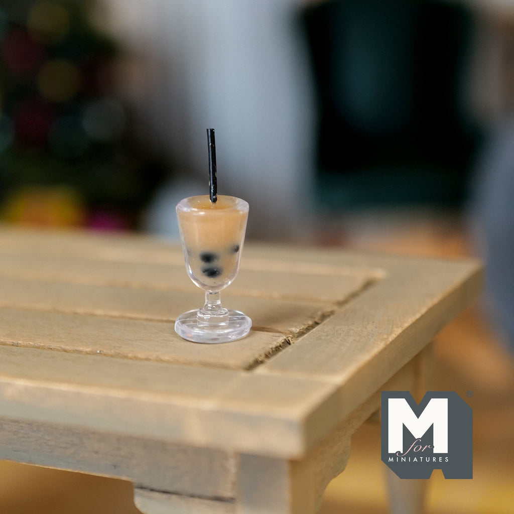 1:12 scale miniature bubble tea in a clear footed cup with black straw and tapioca pearls, shown on a wood table