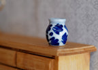 1:12 scale miniature ceramic flower pot with blue floral pattern on white, rounded jar shape, shown on a wood dresser