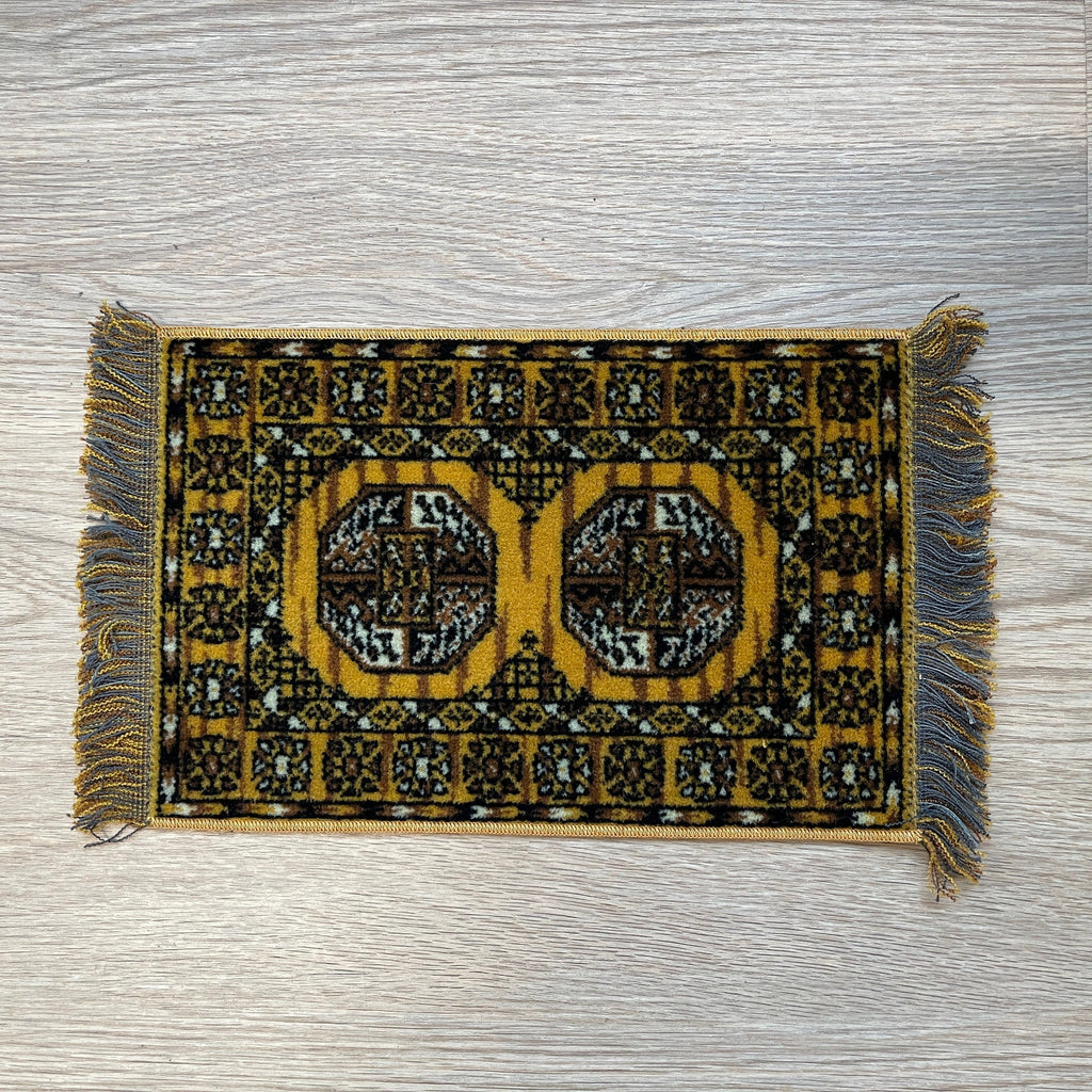 1:12 scale miniature wool medallion area rug in golden yellow with black pattern and gray fringe, on a wood floor