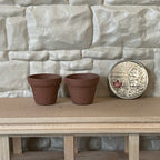 1:12 scale miniature clay flower pots in brown terracotta, set of 2, on a wood shelf beside a coin for scale