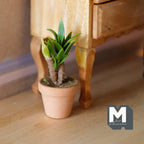 1:12 scale miniature potted strawberry plant in a clay pot with long green leaves, shown on a wood floor