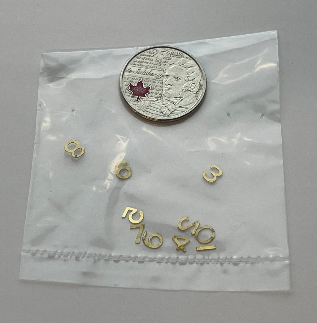 1:12 scale miniature brass house numbers 0 to 9 in gold, set of 10, loose digits shown in a clear bag beside a coin