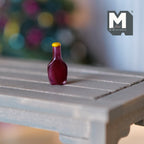 1:12 scale miniature BBQ sauce bottle in dark red brown with a yellow cap, shown on a gray wood table