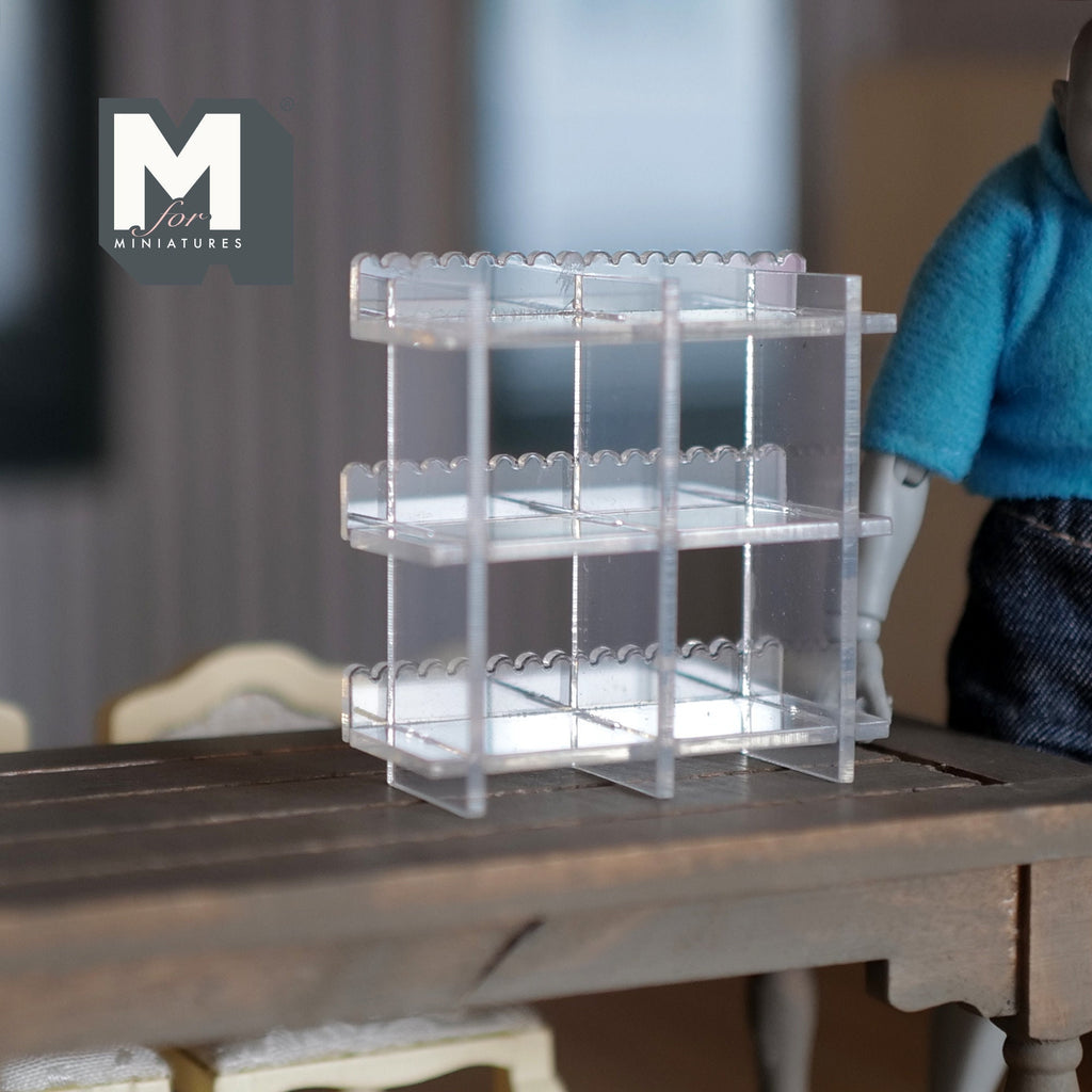 1:12 scale miniature clear acrylic cake display shelf with 3 tiers and scalloped edges, shown on a dark wood table