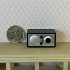 1:12 scale miniature retro tabletop dial radio in black with a silver front, shown on a shelf beside a coin for scale