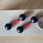 1:12 scale miniature dumbbells in black with red grips, set of 2, shown on a light wood surface beside a coin
