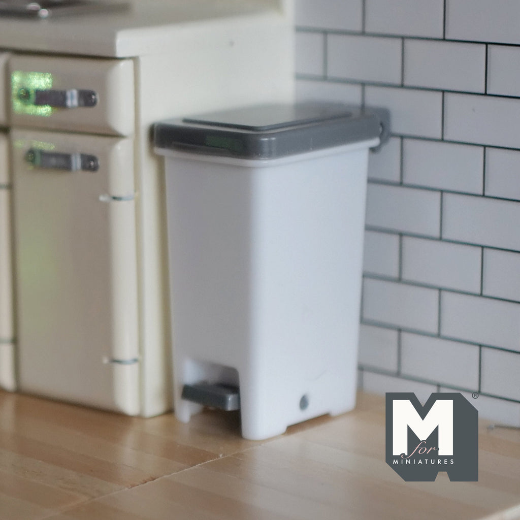 1:12 scale miniature step on trash can with foot pedal, light gray body with darker gray lid, in a tiled kitchen