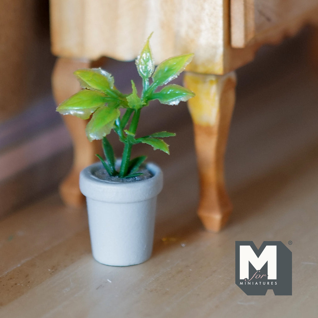 1:12 scale miniature cast resin potted plant with green leaves in a white round pot, shown beside a wood table leg