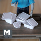 1:12 scale miniature white food containers with lids, set of 4, shown on a dark wood table by a poseable figure