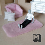 1:12 scale miniature faux sheepskin rug in pink, rectangular, shown on a floor with a jointed figure sitting on it