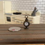 1:12 scale miniature metal antique style table clock in bronze, non working, shown on a wood table beside a coin