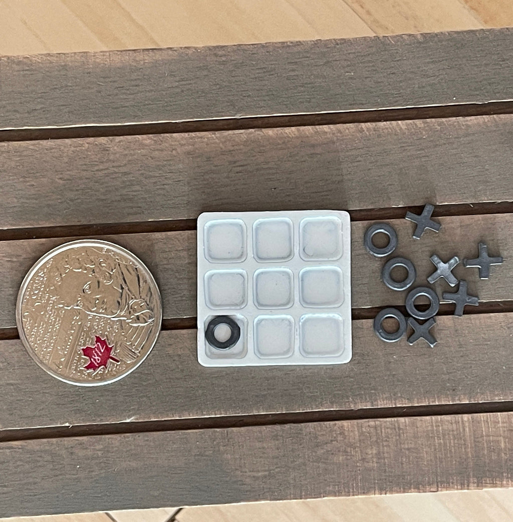 1:12 scale miniature metal tic tac toe set with white tray board and gray X and O pieces, shown beside a coin