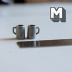 1:12 scale miniature metal mugs in gray with handles, set of 2, shown on a white counter