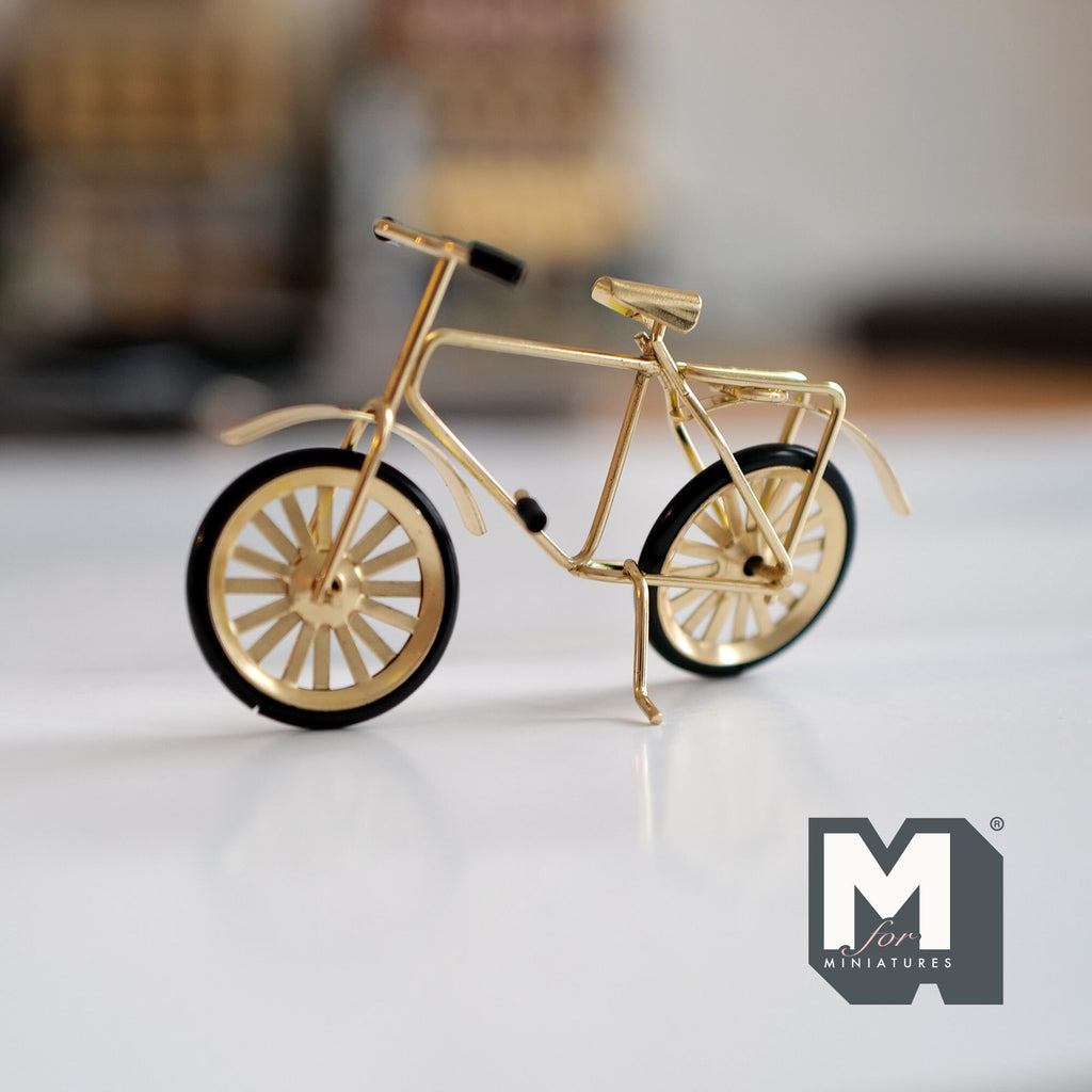 1:12 scale miniature gold metal kid's bicycle with spoked wheels and black tires, standing on a white surface