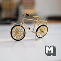 1:12 scale miniature gold metal kid's bicycle with spoked wheels and black tires, standing on a white surface