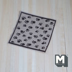 1:12 scale miniature pet blanket in beige with black paw print pattern and dark border, on a wood floor