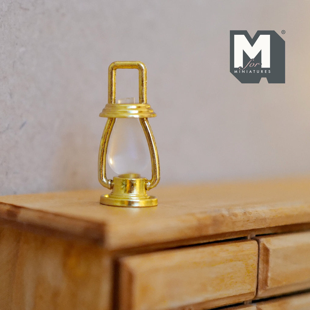 1:12 scale miniature metal hurricane lantern in brass with a ring handle and clear globe, shown on a wood dresser
