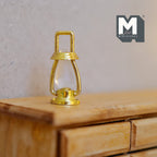 1:12 scale miniature metal hurricane lantern in brass with a ring handle and clear globe, shown on a wood dresser