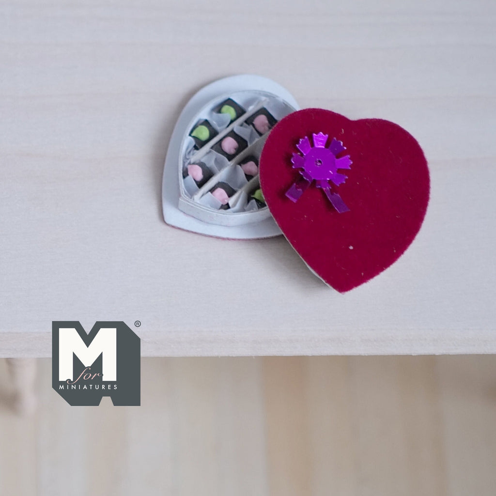 1:12 scale miniature red heart shaped box of chocolates with purple bow on the lid, non edible, lid open on a table