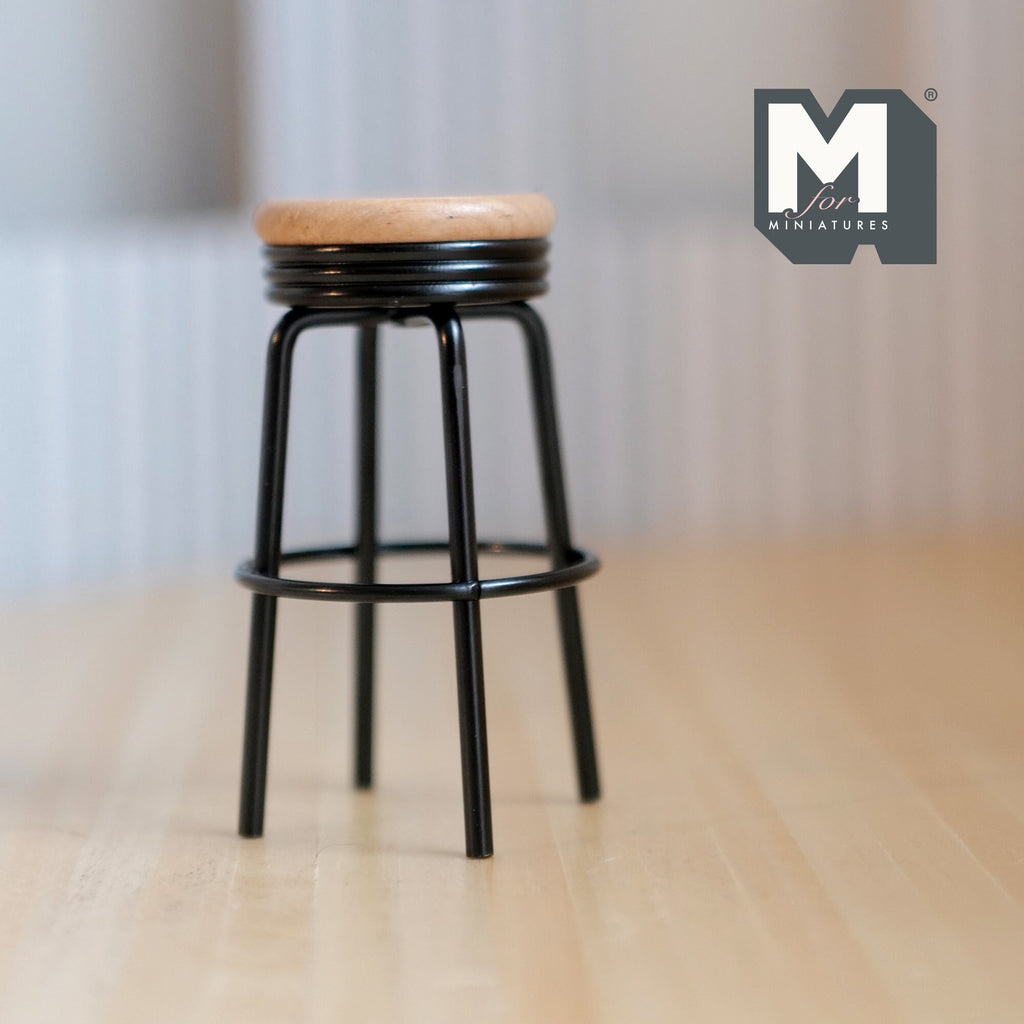 1:12 scale miniature metal bar stool in black with round wood seat and foot ring, shown on a light wood floor