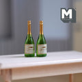 1:12 scale miniature sparkling wine bottles with gold foil tops, set of 2, green bottles shown on a white table