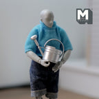 1:12 scale miniature metal watering can in silver with spray nozzle and handle, shown held by a poseable figure