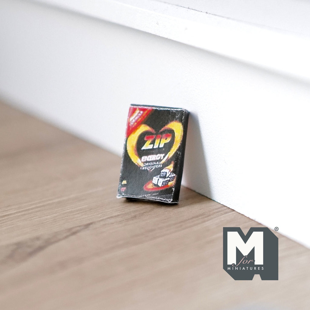 1:12 scale miniature BBQ fire starter box, empty box with black, red and yellow print, shown leaning against a wall