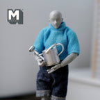 1:12 scale miniature silver metal watering can with sprinkler spout, held by an artist figure in a blue sweater