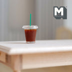 1:6 scale miniature iced coffee cup with clear lid and green straw, shown on a white wood table